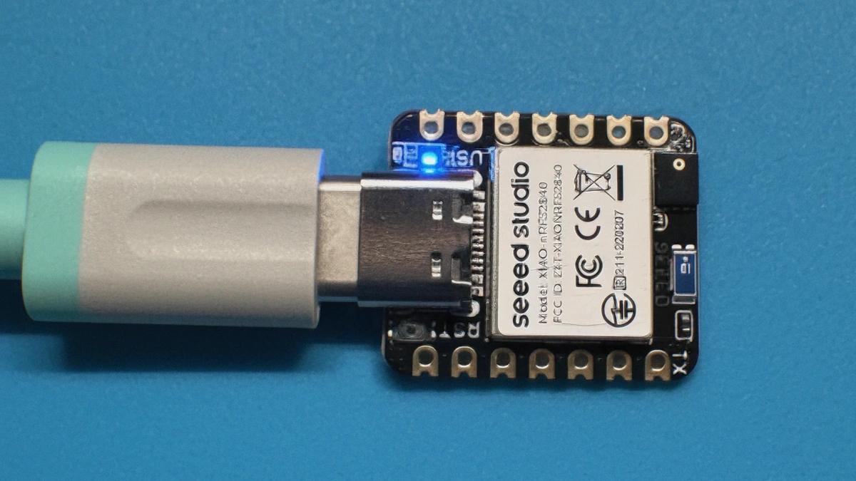 XIAO nRF52840 Sense mit angeschlossenem USB-C-Kabel auf einer blauen Arbeitsmatte.